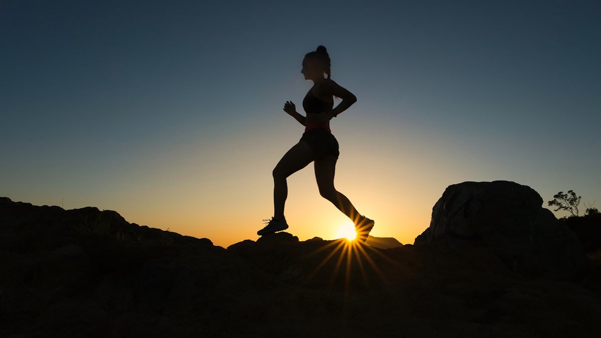A woman runs up a trail during sunset.